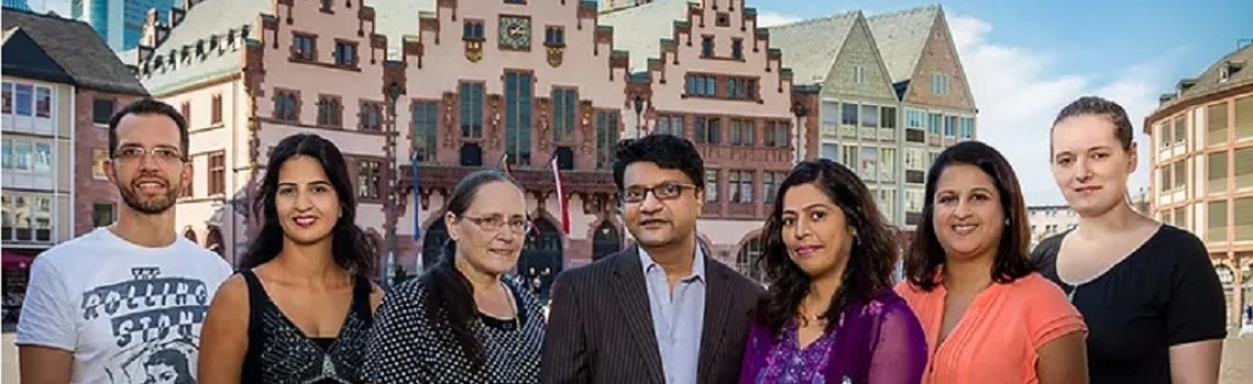 Eine Gruppe von Menschen schaut in die Kamera. Im Hintergrund ist die Frankfurter Altstadt zu sehen.