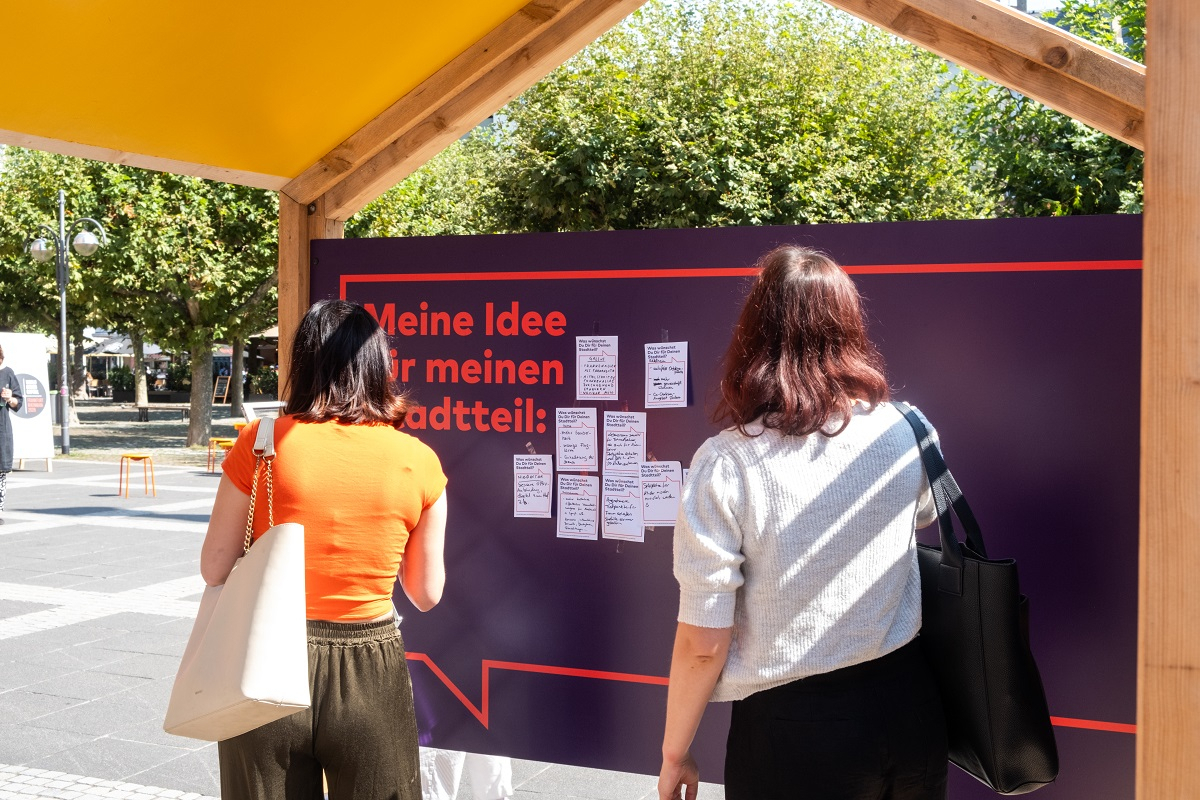 Besucherinnen beschäftigen sich mit der Frage: Was wünscht du dir für deinen Stadtteil? Besucherinnen vor dem Pavillon
