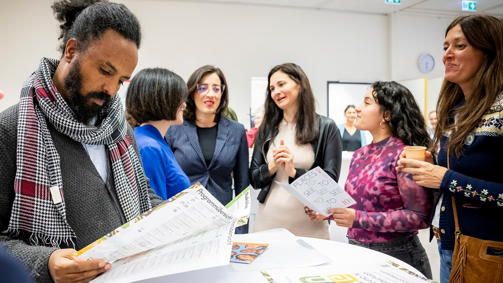 Besucher bei Eröffnungsfeier der Interkulturellen Woche rund um einen Stehtisch mit dem Programmheft 