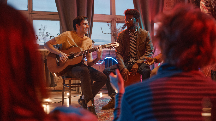 Zwei Personen sitzen mit je einer Gitarre und einem Cachon vor einem Publikum
