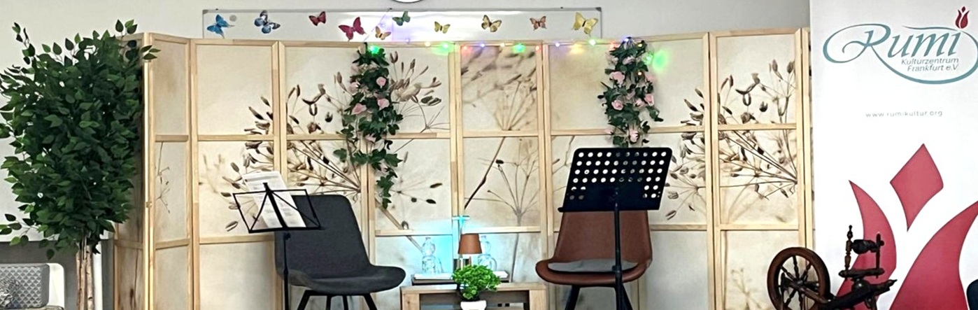 Eine Bühne mit zwei Stühlen, weiteren Gegenständen und einem Roll-up mit dem Rumi-Logo (© Rumi Kulturzentrum Frankfurt)