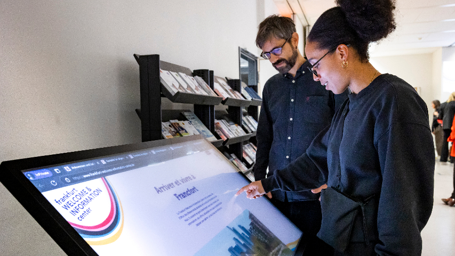 Ein Mann und eine Frau vor dem Touchscreen im FWIC. An dem Screen können sich ratsuchende Besucher:innen neben der persönlichen Beratung im FWIC auch online in 17 Sprachen zu vielen Themen rund um Ankommen und Leben in Frankfurt informieren. (© Stadt Frankfurt am Main, Mara Monetti) Ein Mann und eine Frau vor dem Touchscreen im FWIC, an dem sich Ratsuchende auch online in 17 Sprachen zu vielen Themen informieren können.