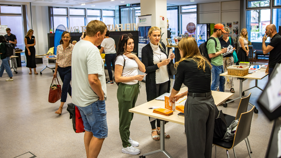 Infomarkt im Frankfurt Welcome & Information Center (FWIC). Das FWIC hat seinen Sitz im Erdgeschoss des stadtRAUMfrankfurt in der Mainzer Landstraße 293 nahe der Galluswarte. (© Stadt Frankfurt am Main, Peter Krausgrill) Infomarkt im Frankfurt Welcome & Information Center mit vielen Personen vor und hinter Ständen von Beratungs-Institutionen
