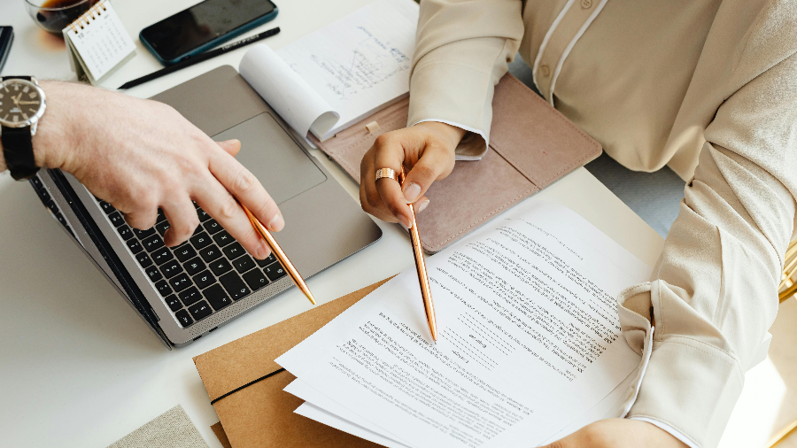 Ausschnitt der Hände und Arme zweier Personen mit Antrag an einem Schreibtisch