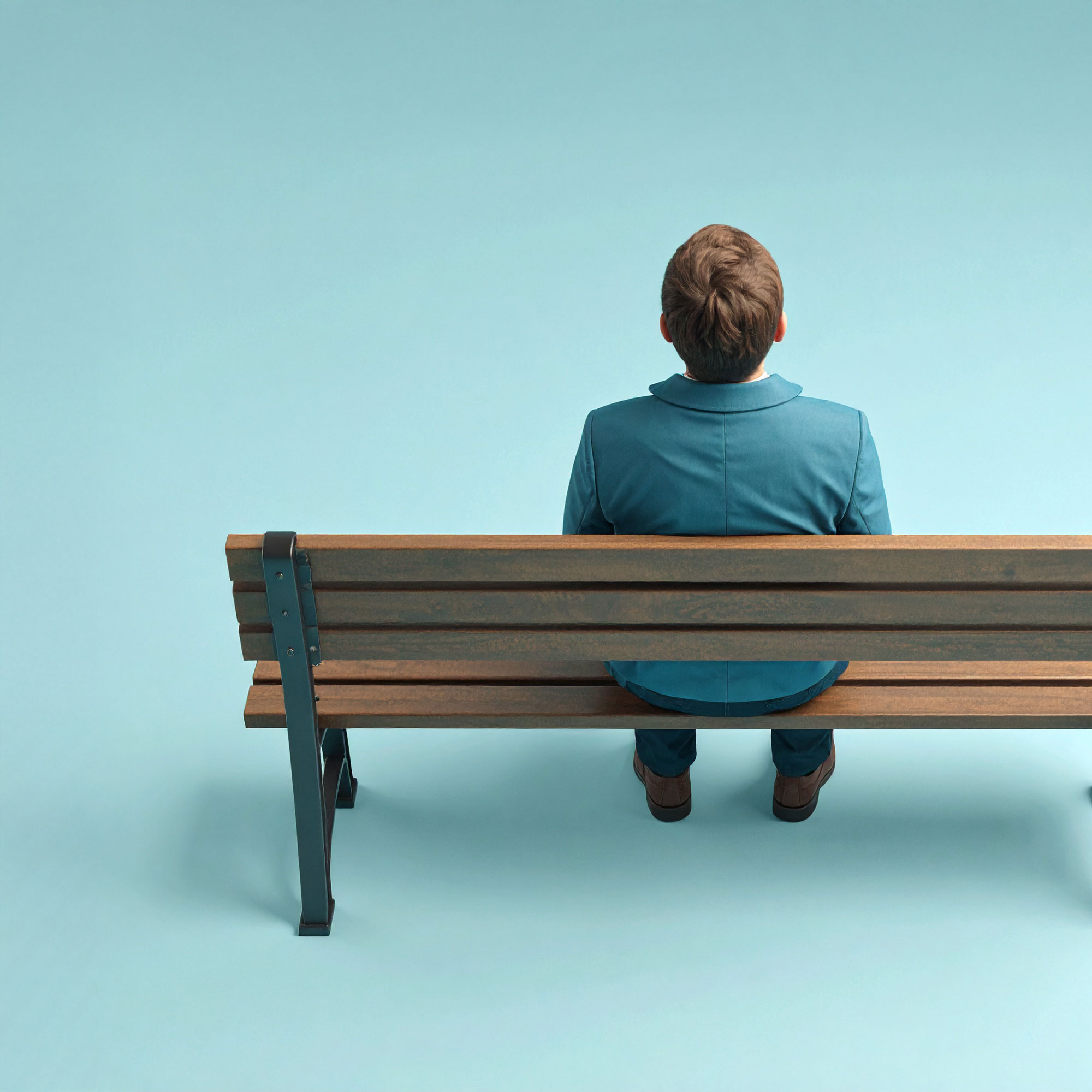 Eine Person alleine sitzend auf einer Bank von hinten