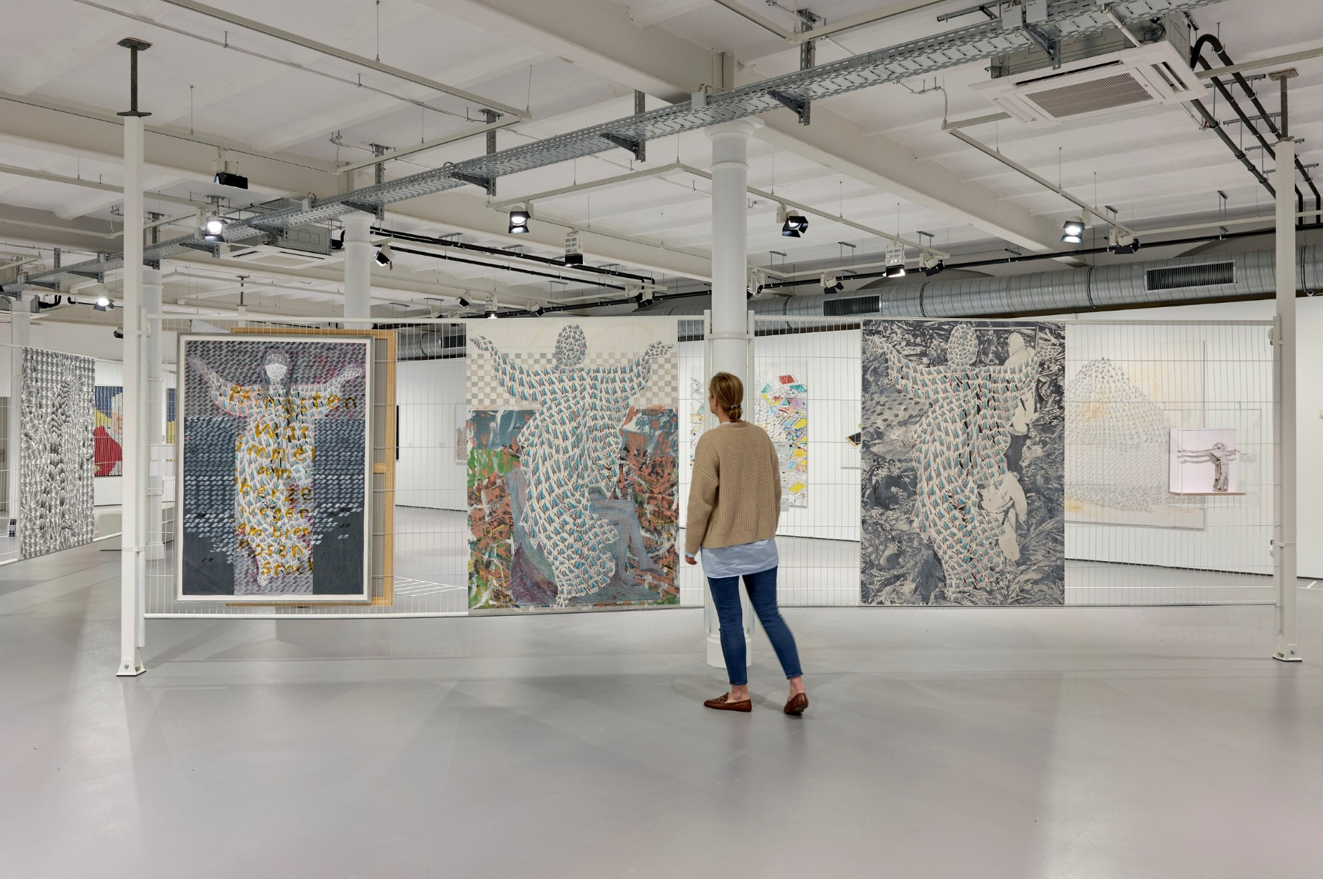 Eine Person steht steht im Ausstellungsraum. Es sind drei große Werke von Thomas Bayrle zu sehen.