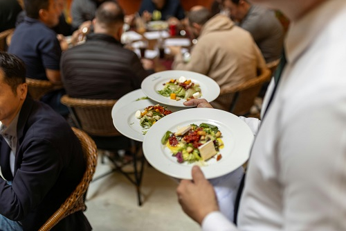 Ein Kellner mit Essenstelleren vor Kulisse mit Gästen