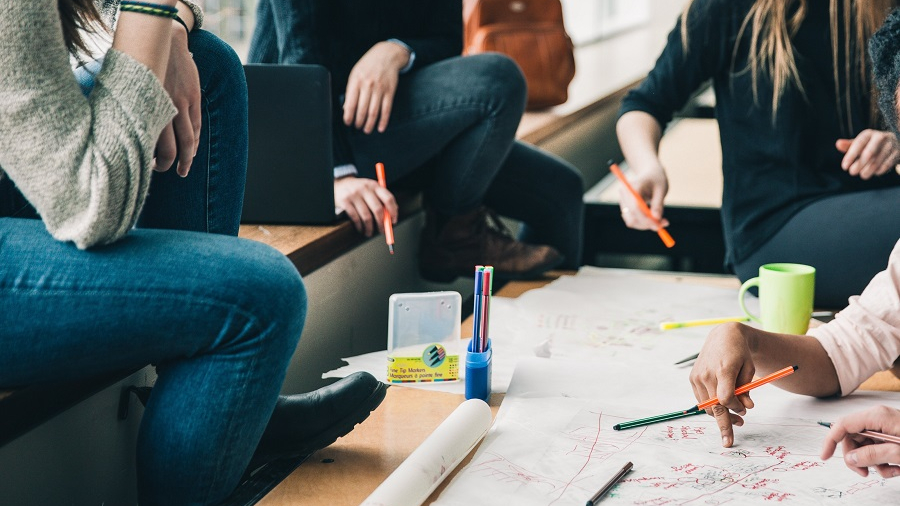 Menschen mit Stiften und Papier sitztend um einen Tisch