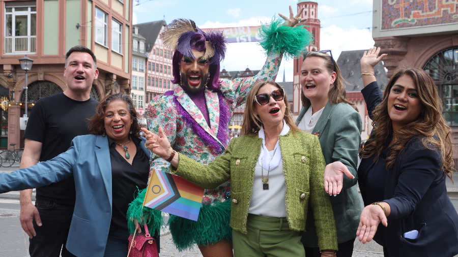 Bei der Präsentation des Pride-Month-Programms: Carsten Gehrig (Aids-Hilfe), Adriana Maximino dos Santos (Verein Aba), Dragkünstler:in Maxima Love, Bürgermeisterin Nargess Eskandari-Grünberg, Julia Meier (Club Cherry), Harpreet Cholia (Stabsstelle Antidiskriminierung). (© Stadt Frankfurt am Main, Maik Reuß)