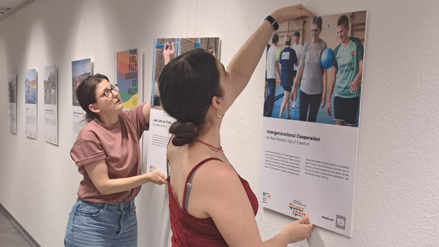 Zwei Personen hängen Bilder der Ausstellung auf
