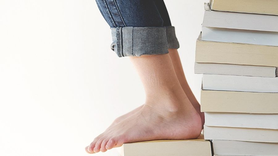 Bücherstapel mit sitzender Person barfus darauf