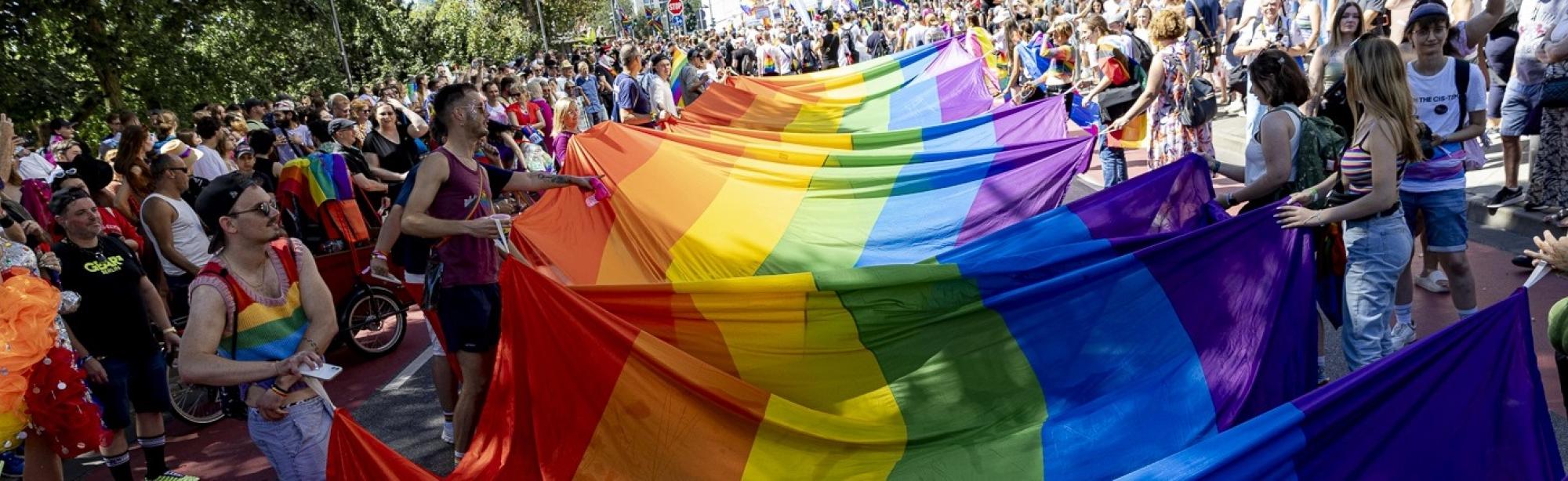 Eine Menschengruppe, die eine riesige Regenbogenflagge in ihrer Mitte ausgebreitet hat (© Stadt Frankfurt, Katarina Ivanisevic)