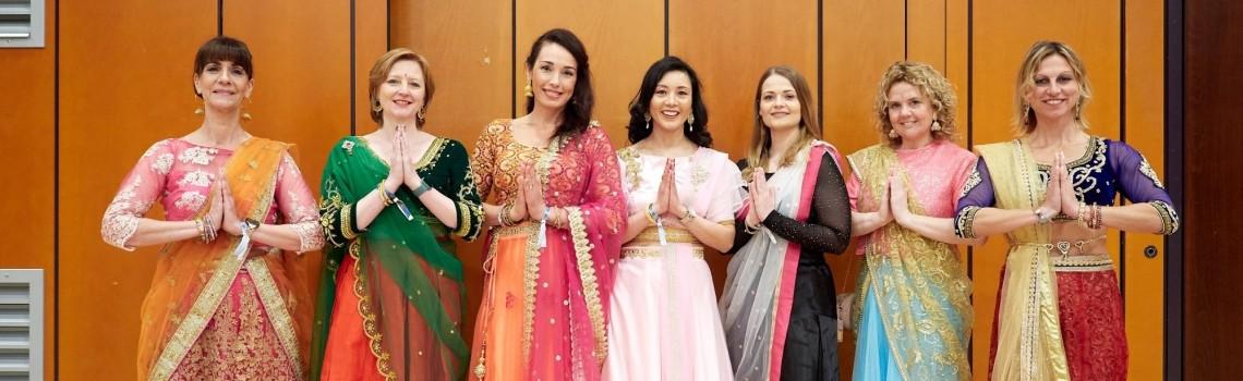 Sieben Frauen stehen in traditionellen Gewändern nebeneinander.